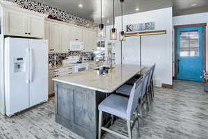 Kitchen featuring white cabinetry, an island with sink, sink, a barn door, and white appliances