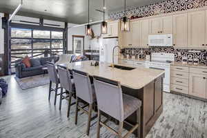 Kitchen with a kitchen island with sink, white appliances, decorative light fixtures, and a breakfast bar