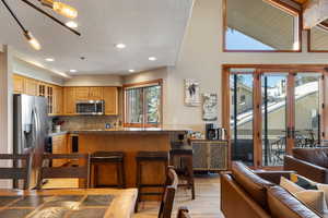 Kitchen with a breakfast bar, tasteful backsplash, dark stone countertops, stainless steel appliances, and light hardwood / wood-style floors