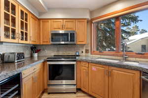 Kitchen featuring wine cooler, sink, stainless steel appliances, and dark stone counters