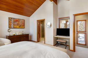 Carpeted bedroom featuring wooden ceiling, high vaulted ceiling, and ensuite bath