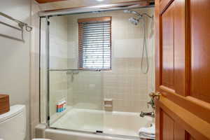 Bathroom with shower / bath combination with glass door and toilet