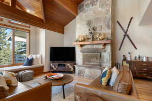 Living room featuring a stone fireplace, high vaulted ceiling, light hardwood / wood-style flooring, and wooden ceiling