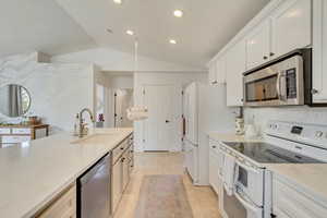 Kitchen with sink, light stone countertops, white cabinets, and appliances with stainless steel finishes