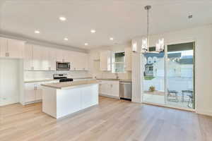 Kitchen with decorative light fixtures, white cabinets, a center island, stainless steel appliances, and a healthy amount of sunlight