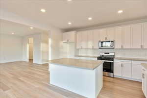 Kitchen with light hardwood / wood-style flooring, a kitchen island with gray quartz counter tops, white cabinets, and appliances with stainless steel finishes