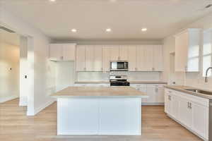 Kitchen with gray quartz counter tops, a center island, appliances with stainless steel finishes, light hardwood / wood-style floors, and white cabinets