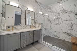 Bathroom featuring tiled shower, vanity, and tile walls