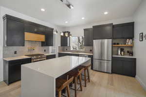 Kitchen with a breakfast bar, hanging light fixtures, premium appliances, light hardwood / wood-style floors, and a kitchen island