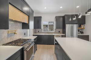 Kitchen featuring sink, premium appliances, decorative backsplash, decorative light fixtures, and light wood-type flooring