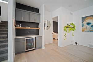 Bar with beverage cooler, gray cabinets, decorative backsplash, and light wood-type flooring