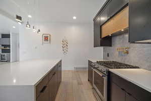 Kitchen with high end range, hanging light fixtures, tasteful backsplash, light hardwood / wood-style floors, and beverage cooler