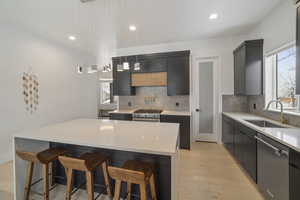 Kitchen featuring a kitchen island, sink, a breakfast bar area, hanging light fixtures, and stainless steel appliances