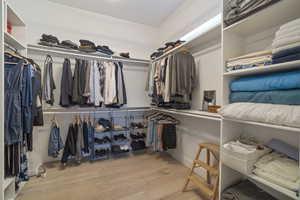 Walk in closet with light hardwood / wood-style flooring