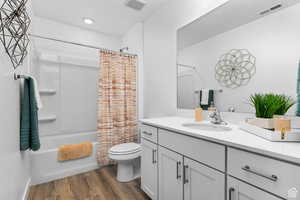 Full bathroom featuring vanity, hardwood / wood-style floors, shower / bath combo with shower curtain, and toilet