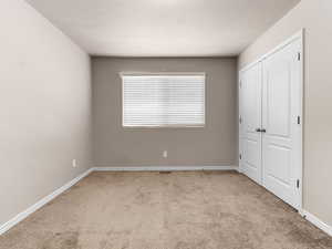 Unfurnished bedroom featuring light colored carpet, a closet, and a textured ceiling