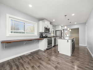 Kitchen with white cabinetry, hanging light fixtures, a breakfast bar, and appliances with stainless steel finishes