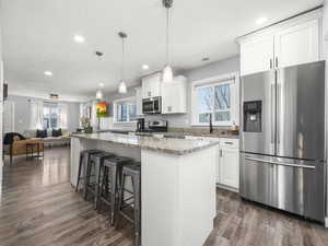 Kitchen with stainless steel appliances, a center island, white cabinets, and decorative light fixtures