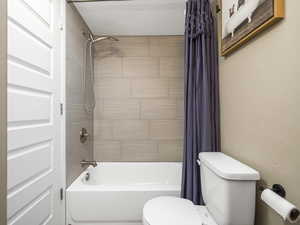 Bathroom featuring shower / tub combo with curtain, toilet, and a textured ceiling