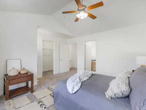 Carpeted bedroom featuring ensuite bath, ceiling fan, vaulted ceiling, a walk in closet, and a closet