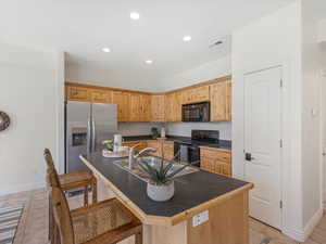 Kitchen featuring light tile patterned floors, sink, a kitchen island with sink, black appliances, and light brown cabinets