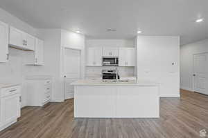 Kitchen with stainless steel appliances, a kitchen island with sink, sink, and white cabinets