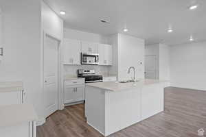 Kitchen with an island with sink, white cabinetry, sink, stainless steel appliances, and light hardwood / wood-style flooring