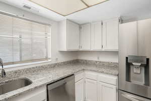 Kitchen with white cabinetry, sink, light stone counters, and stainless steel appliances