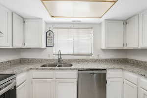 Kitchen with stainless steel appliances, sink, white cabinets, and light stone counters