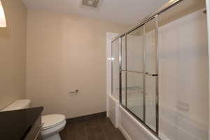 Full bathroom with bath / shower combo with glass door, tile patterned floors, toilet, and vanity