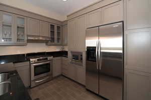 Kitchen with stainless steel appliances, dark tile patterned flooring, and gray cabinetry