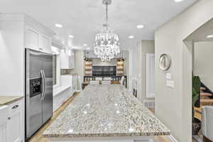 Kitchen featuring stainless steel refrigerator with ice dispenser, light stone counters, a center island, light wood-type flooring, and white cabinets