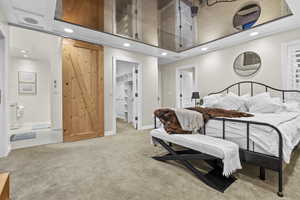 Bedroom featuring ensuite bath, a walk in closet, light colored carpet, and a barn door