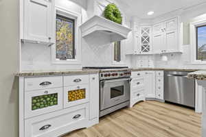 Kitchen featuring white cabinetry, stainless steel appliances, light stone countertops, and light wood-type flooring