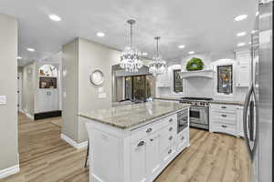 Kitchen with pendant lighting, white cabinetry, a center island, stainless steel appliances, and light hardwood / wood-style flooring