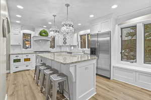 Kitchen featuring appliances with stainless steel finishes, decorative light fixtures, white cabinets, a center island, and light wood-type flooring