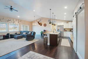 Kitchen featuring a breakfast bar, stainless steel fridge with ice dispenser, a center island with sink, pendant lighting, and white cabinets