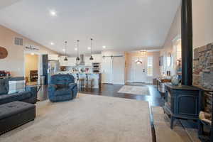 Living room featuring high vaulted ceiling, a barn door, hardwood / wood-style floors, and a wood stove