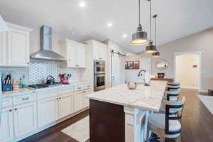 Kitchen with a kitchen island with sink, a barn door, wall chimney exhaust hood, and appliances with stainless steel finishes