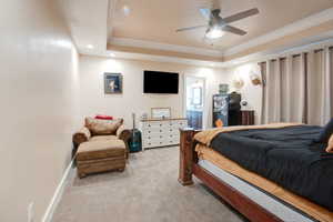 Bedroom with ensuite bath, ornamental molding, a raised ceiling, and light carpet