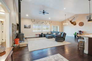 Living room featuring lofted ceiling, dark wood-type flooring, ceiling fan, and a wood stove