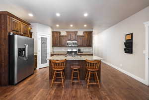 Kitchen with a breakfast bar area, appliances with stainless steel finishes, dark wood-type flooring, and a center island with sink