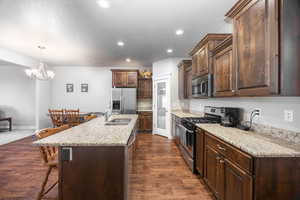 Kitchen with dark wood-type flooring, a kitchen bar, sink, a center island with sink, and appliances with stainless steel finishes