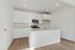 Kitchen featuring white cabinetry, light hardwood / wood-style flooring, stainless steel appliances, and a center island with sink