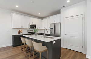 Kitchen featuring sink, appliances with stainless steel finishes, white cabinetry, a kitchen breakfast bar, and a center island with sink