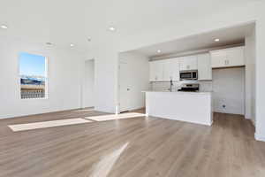 Kitchen featuring a center island with sink, appliances with stainless steel finishes, white cabinets, light hardwood / wood-style floors, and backsplash