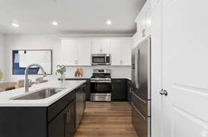 Kitchen with sink, dark wood-type flooring, appliances with stainless steel finishes, white cabinetry, and an island with sink