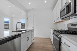 Kitchen featuring stainless steel appliances, light hardwood / wood-style floors, sink, and white cabinets