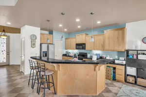 Kitchen with fridge with ice dispenser, pendant lighting, a kitchen island with sink, and light brown cabinets