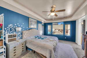 Bedroom featuring a raised ceiling, light colored carpet, and ceiling fan